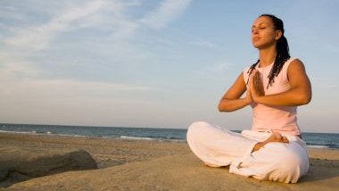 Imagem de uma mulher sentada próximo à praia fazendo sua meditação para o início do ano que se inicia.
