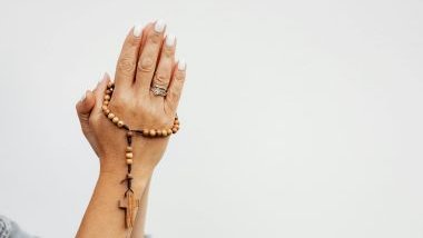 Imagem das mãos unidas de uma mulher segurando um terço de madeira.