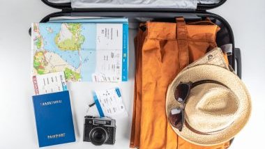 Imagem de uma mala de viagens aberta, contendo: roupas, passaporte, chapéu, óculos de sol, camêra fotográfica e um mapa com os destinos.