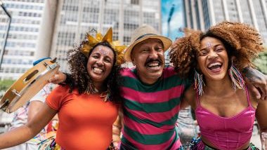 Imagem de um homem e duas mulheres pulando carnaval de rua.