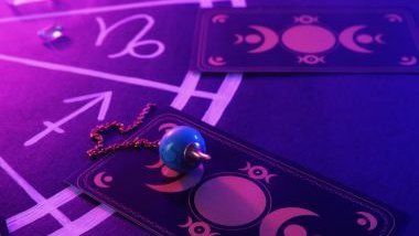 Imagem de uma mandala na cor roxa. Sobre ela, algumas cartas, cristais e um pêndulo de pedra azul.