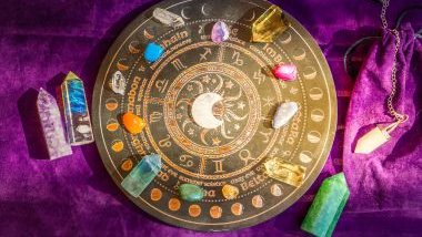 Imagem de uma mandala astrológica na cor dourada, ao centro dela, o sol e a lua. Ela está sobre um tecido roxo e junto com ela, pedras e cristais coloridos.