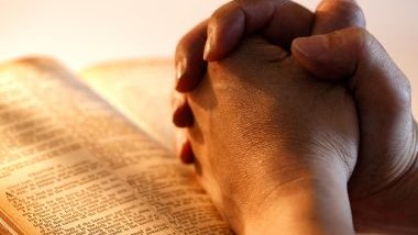 Imagem das mãos unidas em sinal de oração sobre uma bíblia.