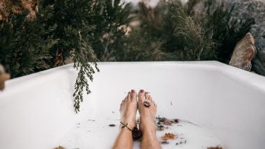 Imagem dos pés de uma mulher com as unhas pintadas de vermelho dentro de uma banheira com flores e água, simbolizando o ritual de um banho espiritual.