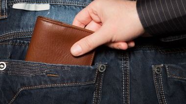 Imagem da mão de um homem, roubando uma carteira dentro do bolso de uma calça jeans.