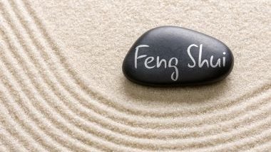 Imagem de uma pedra preta sobre uma areia branca. Na pedra está escrito a palavra:  Feng Shui.