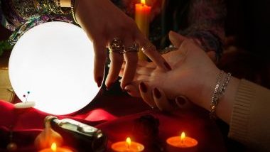 Imagem de uma cigana, fazendo leitura na mão de uma mulher sobre uma mesa com uma luz em formato de lua cheia, velas e uma toalha vermelha de cetim.