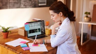 Imagem de uma mulher em sua mesa de trabalho, escrevendo em sua agenda e também em vários post-its, simbolizando uma pessoa detalhista.