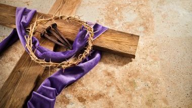 Imagem de uma cruz feita de madeira, com a cruz de espinhos, três pregos e uma faixa roxa, simbolizando a Semana Santa.