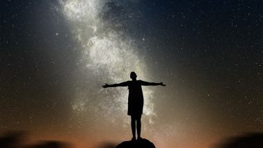 Kirill_Savenko / Getty Images / Canva Imagem de um homem sobre uma pedra, olhando para o universo de braços abertos.