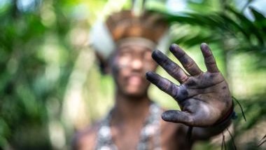 Imagem de um indígena no meio da selva. Em destaque sua mão pintada na cor preta. A foto traz o conceito do Caboclo Ventania na Umbanda.