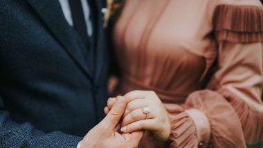 Imagem de um casal. O homem usa um terno azul e a mulher um lindo vestido marrom. Ele segura a mão dela com amor e carinho, simbolizando o melhor marido.
