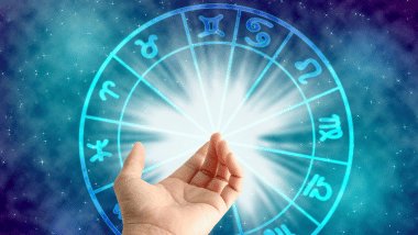 No foco da imagem, há uma Roda do Zodíaco e, na frente dela, há uma mão esticada de uma pessoa.