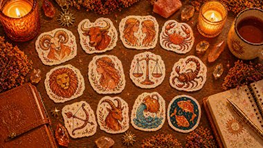 Flat lay acolhedor em tons de laranja com adesivos dos signos espalhados sobre mesa de madeira, cercados por velas, cristais e objetos místicos.