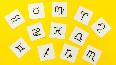 Cada símbolo de um signo do zodíaco está desenhado em um pedaço de papel. Os papéis estão espalhados em cima de um fundo amarelo.