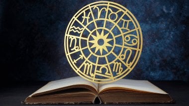 No centro da imagem, há uma Roda do Zodíaco e, embaixo dela, há um livro aberto.