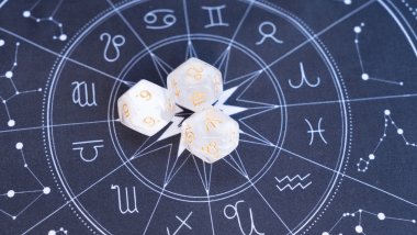 No foco da imagem, há uma Roda do Zodíaco e, em cima dela, há três dados com os símbolos dos signos e números.