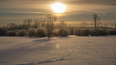 Imagem de um campo coberto com neve, ao fundo um lindo pôr do Sol, simbolizando o Solstício de inverno.