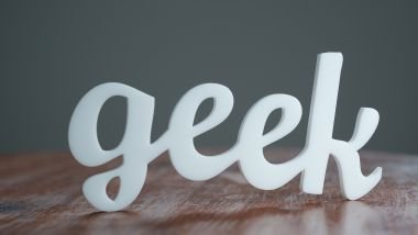 Imagem da palavra geek escrito em letras brancas disposta sobre uma mesa de madeira.