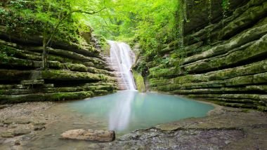 Imagem de uma linda cachoeira, desaguando em um lago azul claro dentro de uma floresta.