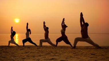 Imagem de várias pessoas praticando yoga na areia da praia em um lindo final de tarde.