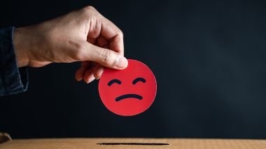 Imagem de uma mão segurando um emoji com a cara de pessoa ruim.
