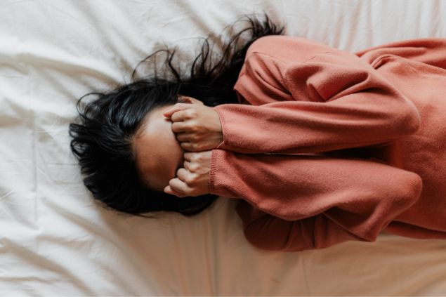 mulher triste deitada na cama cobrindo o rosto