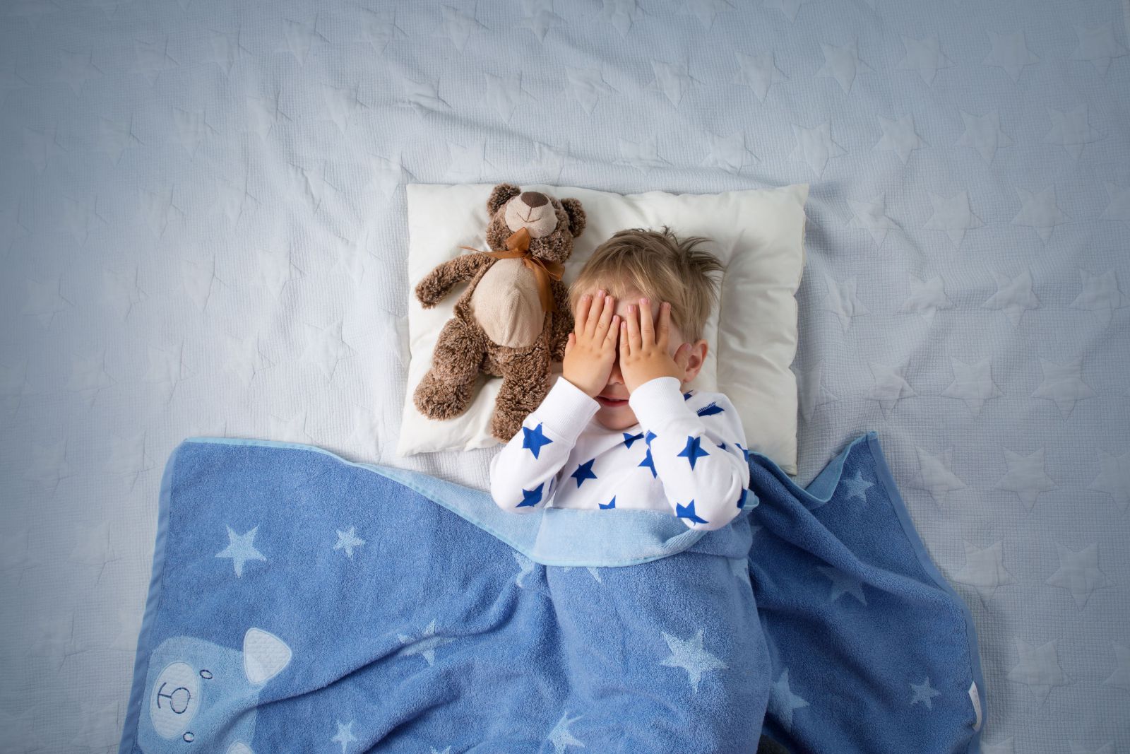 Bebê chorando na cama com as mãos no rosto