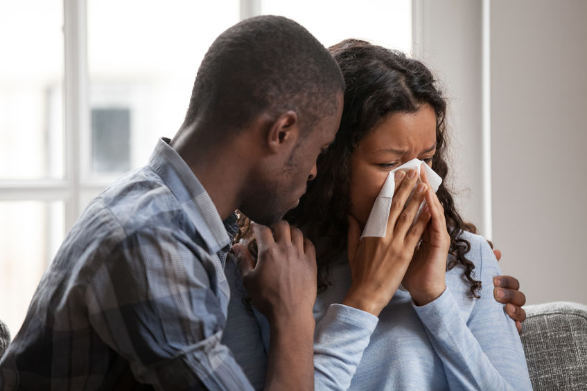 Mulher negra chorando e homem negro a consolando.
