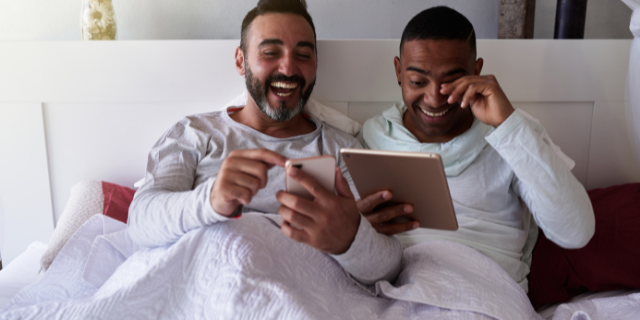 Casal rindo na cama mexendo nos celulares