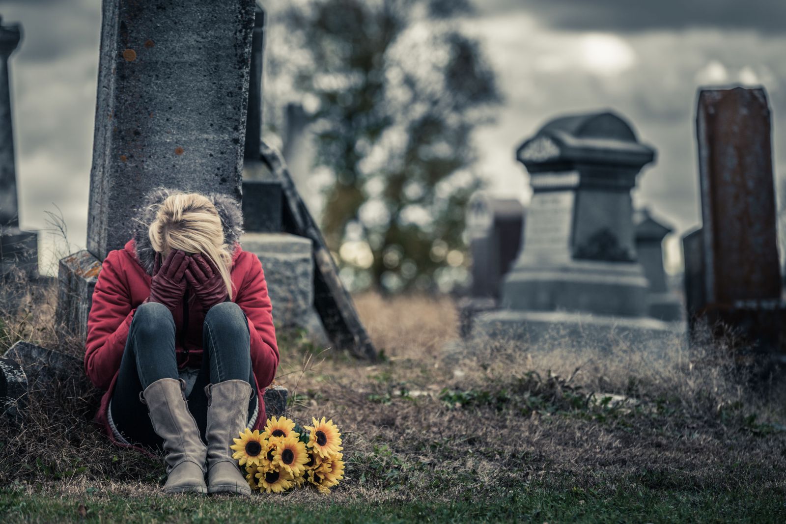 Mulher sentada em frente a uma lápide com as mãos no rosto