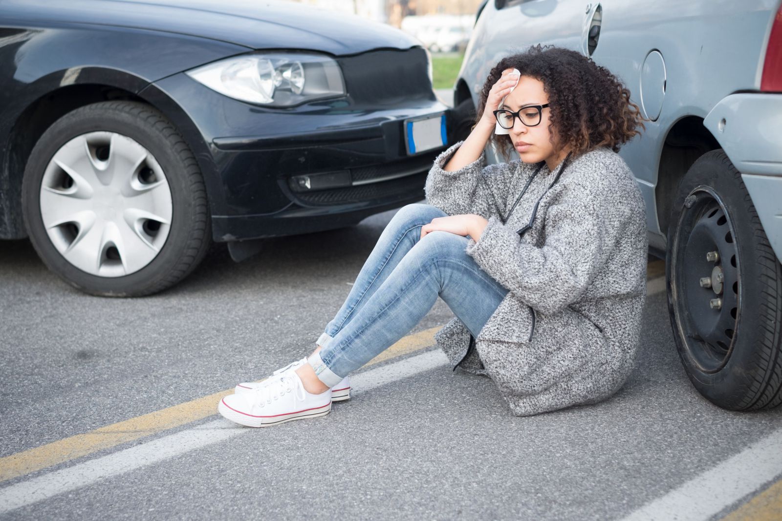 Mulher sentada na rua ao lado de um carro