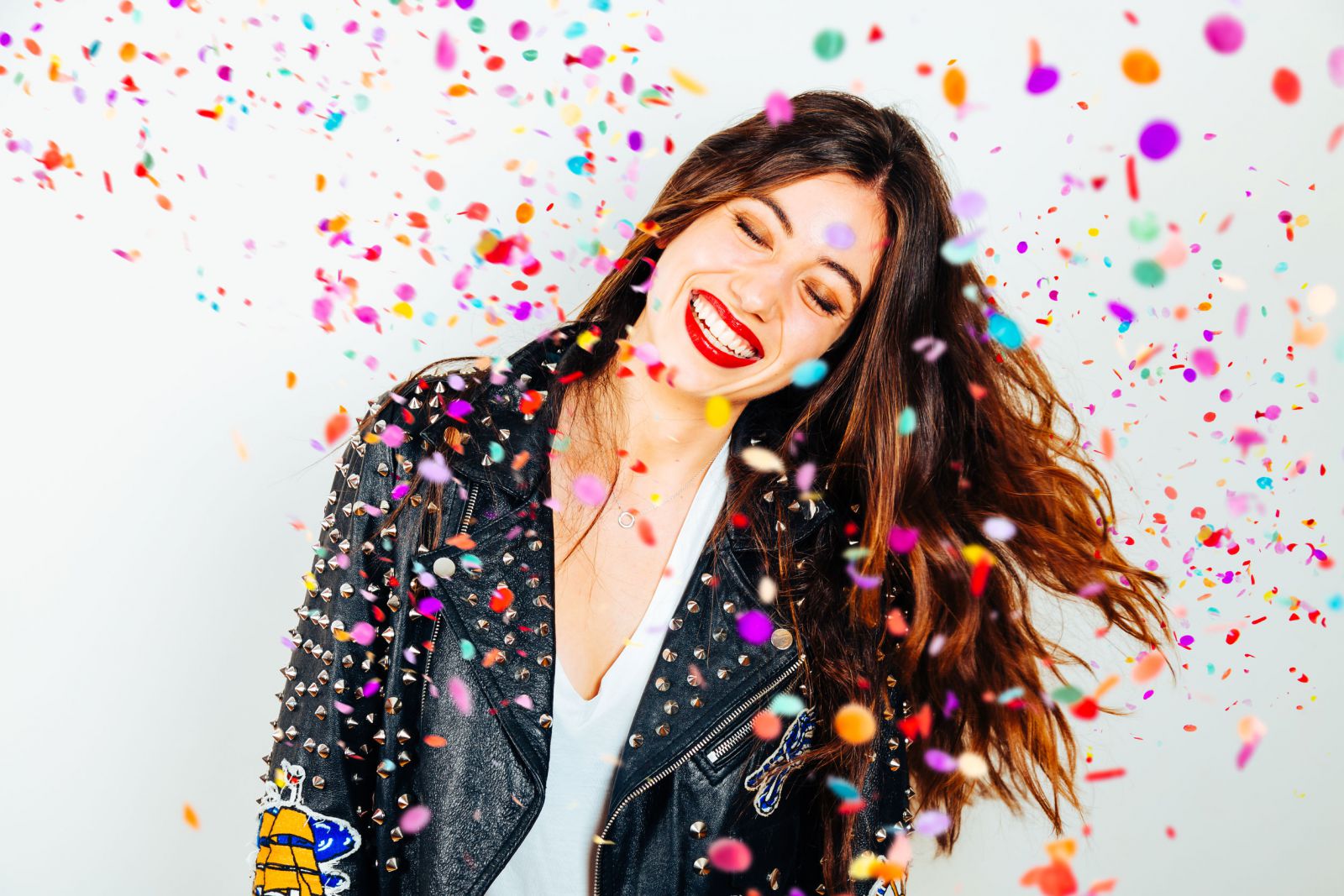 Mulher em pé sorrindo em meio a confetes de aniversário caindo.