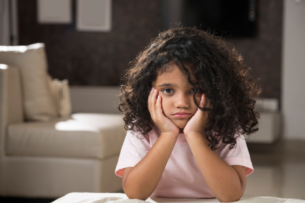 Menina com olhar triste apoiada com o queixo nas duas mãos 