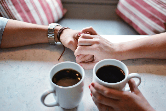 Casal bebendo café com as mãos dadas. 