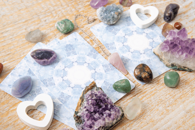 Algumas cartas de Tarot viradas para baixo estão em destaque na imagem. Ao lado, há cristais e outros objetos.