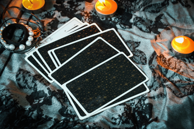 Algumas cartas de Tarot viradas para baixo estão em destaque na imagem. Ao lado, há velas e outros objetos.