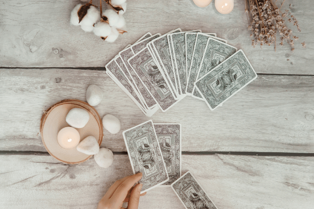 Изображения пользователя annu1tochka / Canva Algumas cartas de Tarot viradas para baixo estão em destaque na imagem. Ao lado, há velas e outros objetos.