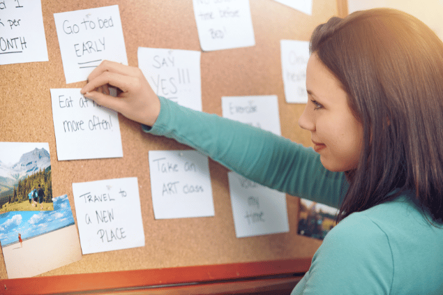 Mulher definindo suas metas em post-its em um quadro de madeira.