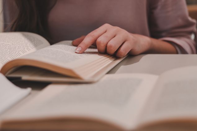 Imagem apenas da mão de uma pessoa apontando para um livro enquanto faz a leitura
