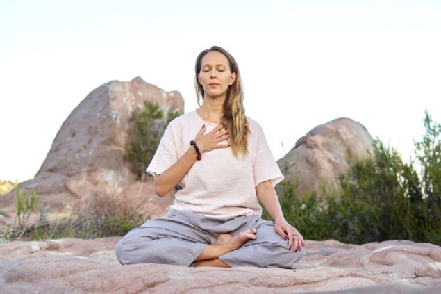 Mulher meditando ao ar livre com os olhos fechados e mão no coração