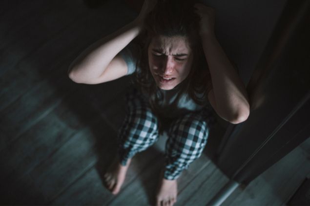 Pessoa com as mãos na cabeça, com expressão de raiva, sentada no chão