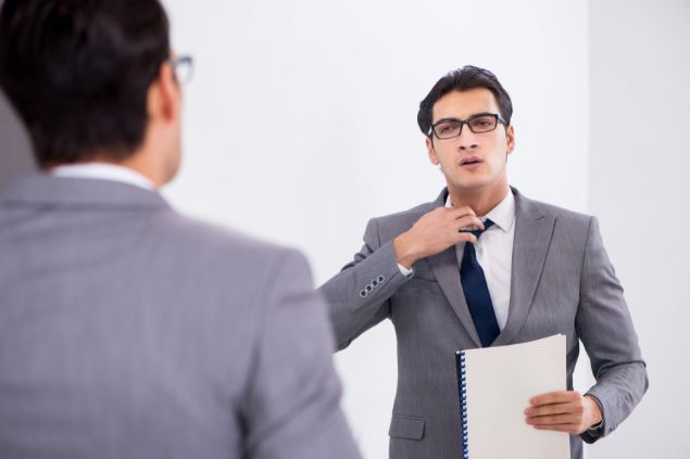Homem com a mão na gravata, tentando falar na frente do espelho
