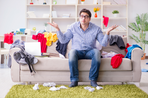 Homem no meio de uma sala bagunçada, com roupas por todo o lugar