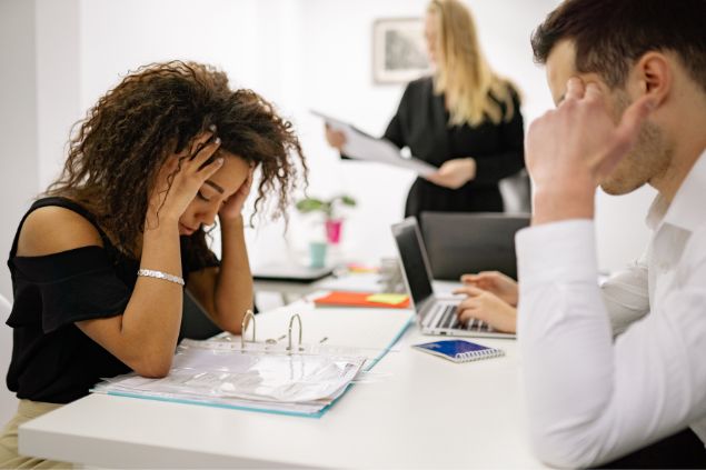 Mulher exausta em frente à mesa com seus colegas de trabalho