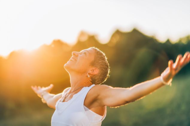 Imagem de uma mulher olhando para o alto e sorrindo com a luz do sol refletida em seu rosto