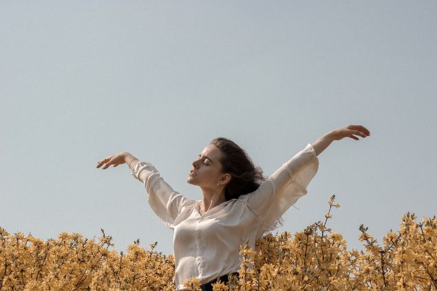 Imagem de uma mulher no meio de um campo com os braços abertos e os olhos fechados, com semblante de tranquilidade