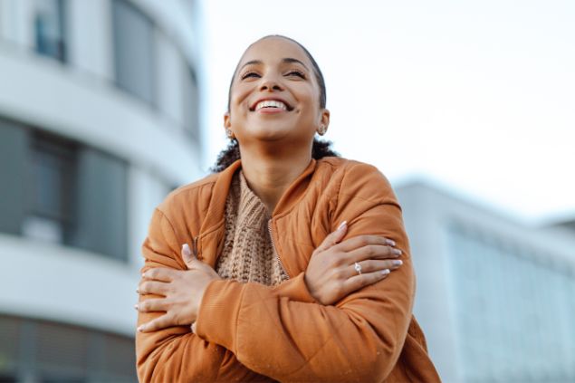 Imagem de uma mulher sorrindo e abraçando a si mesma ao ar livre