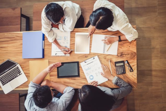 Imagem de quatro pessoas sentadas em uma mesa, fazendo projetos.