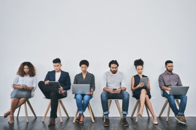 Imagem de 6 pessoas sentadas em cadeiras como se estivessem em uma sala de espera uns com notebook na mão outros com celulares